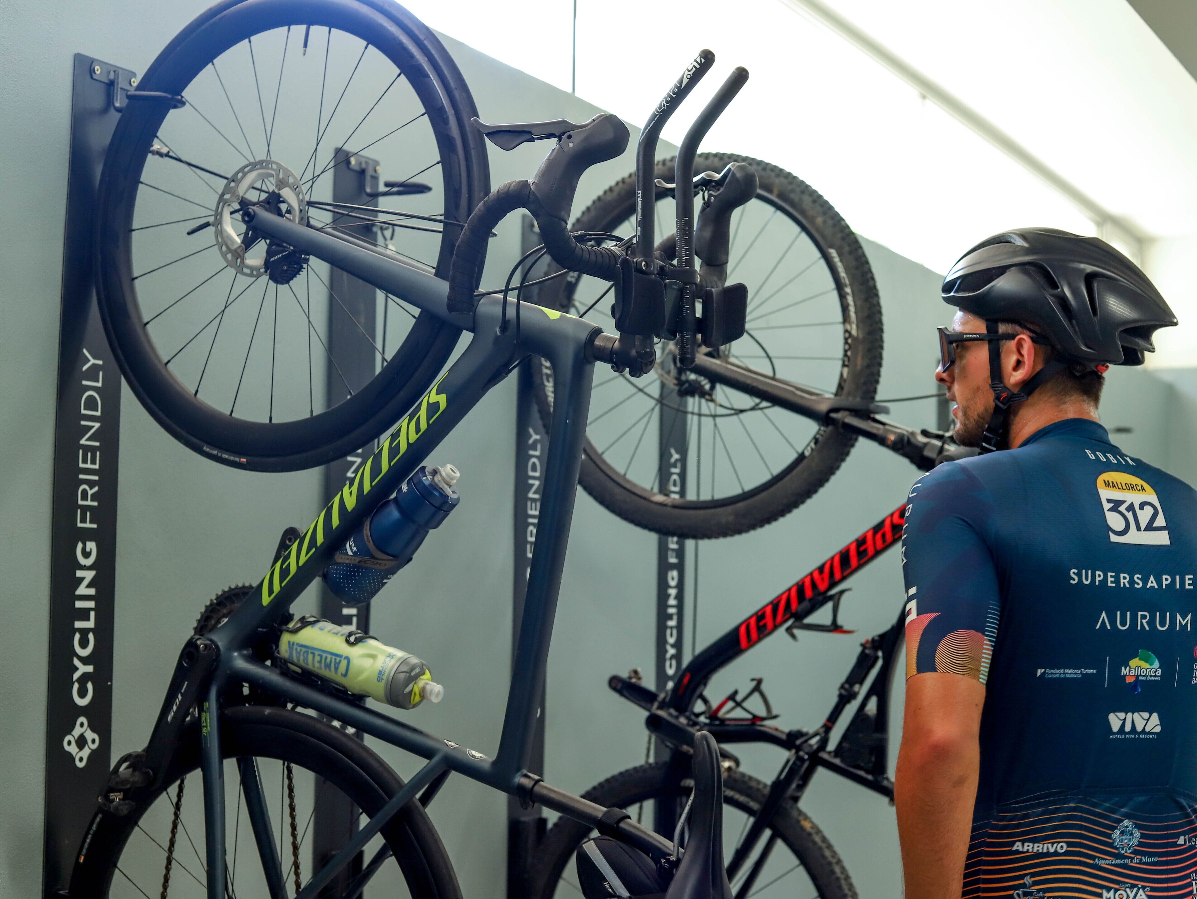 A cyclist with a helmet and cycling gear, a bicycle mounted on a wall, and a water bottle on the bike.