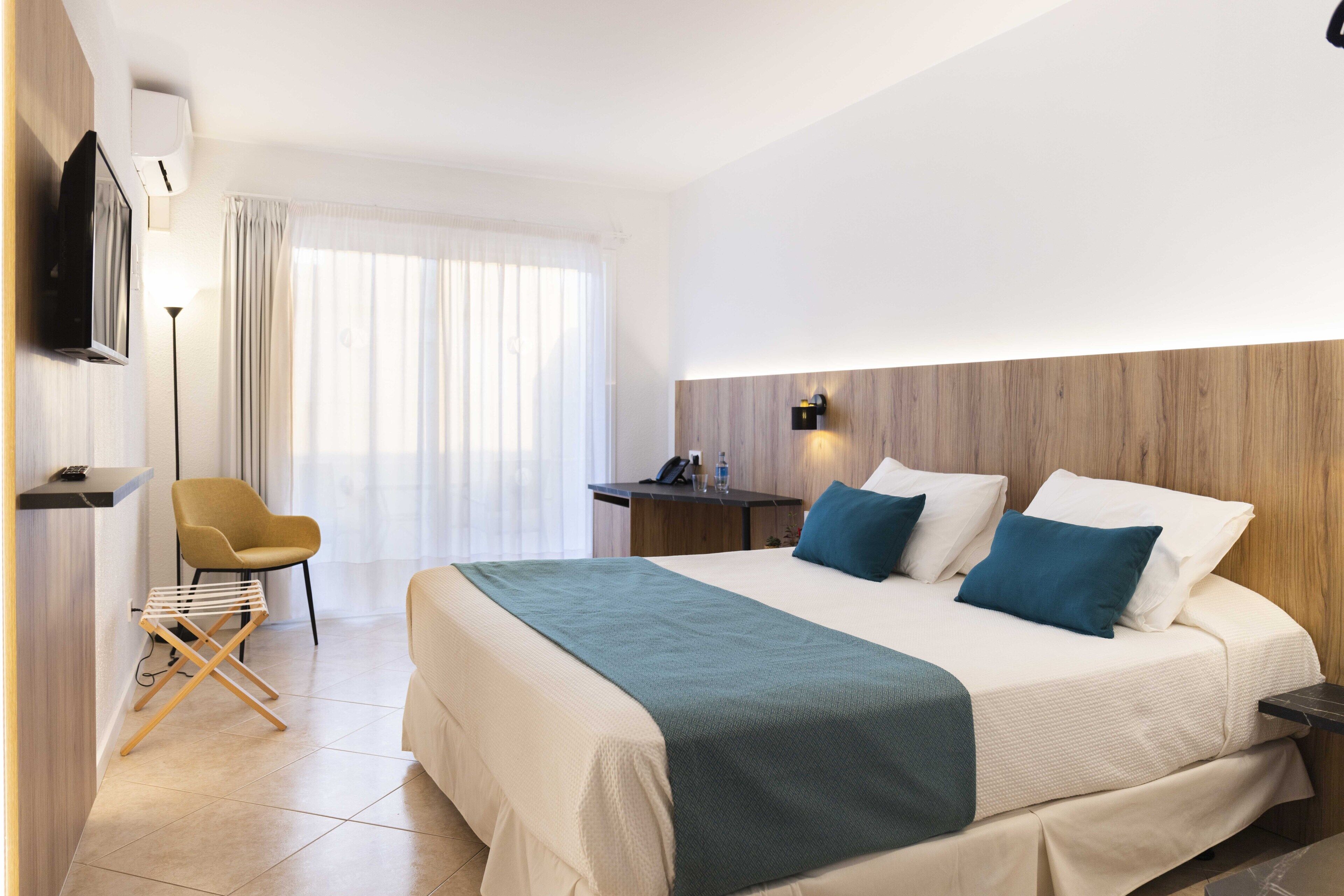 Ein modernes Hotelzimmer mit einem großen Bett, einem Schreibtisch, einem Stuhl und einem an der Wand befestigten Fernseher.
