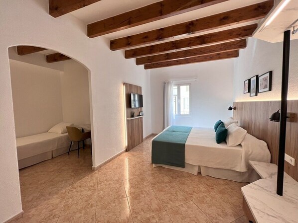 Ein Schlafzimmer mit Bett, Sessel, Schreibtisch und Fernseher.