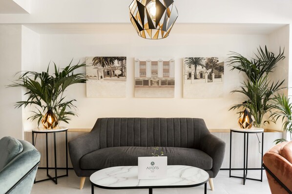 A modern living room with a grey sofa, a marble coffee table, and two side tables with plants.