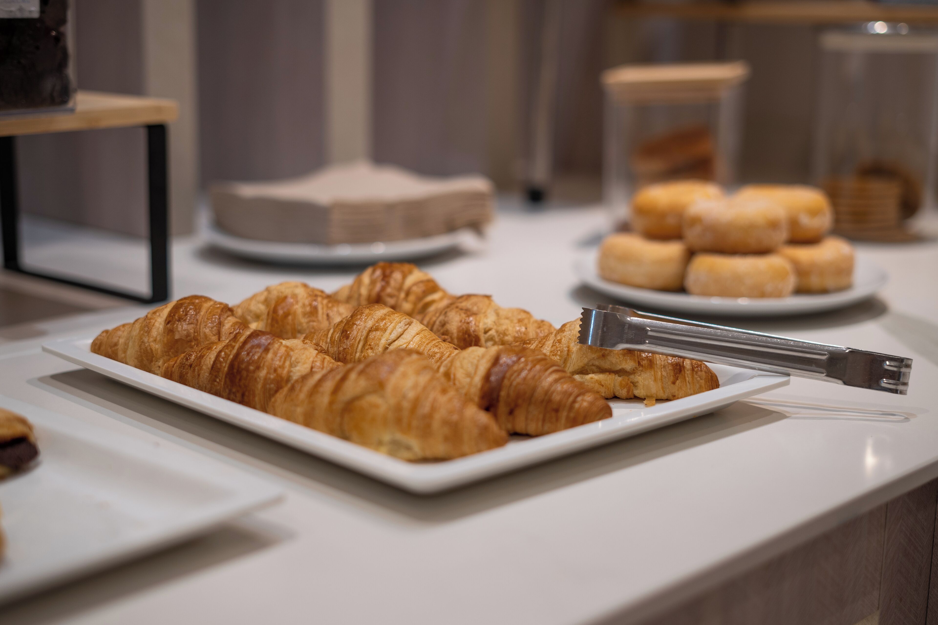 A buffet table with various pastries and bread, including croissants and rolls, arranged on white plates.