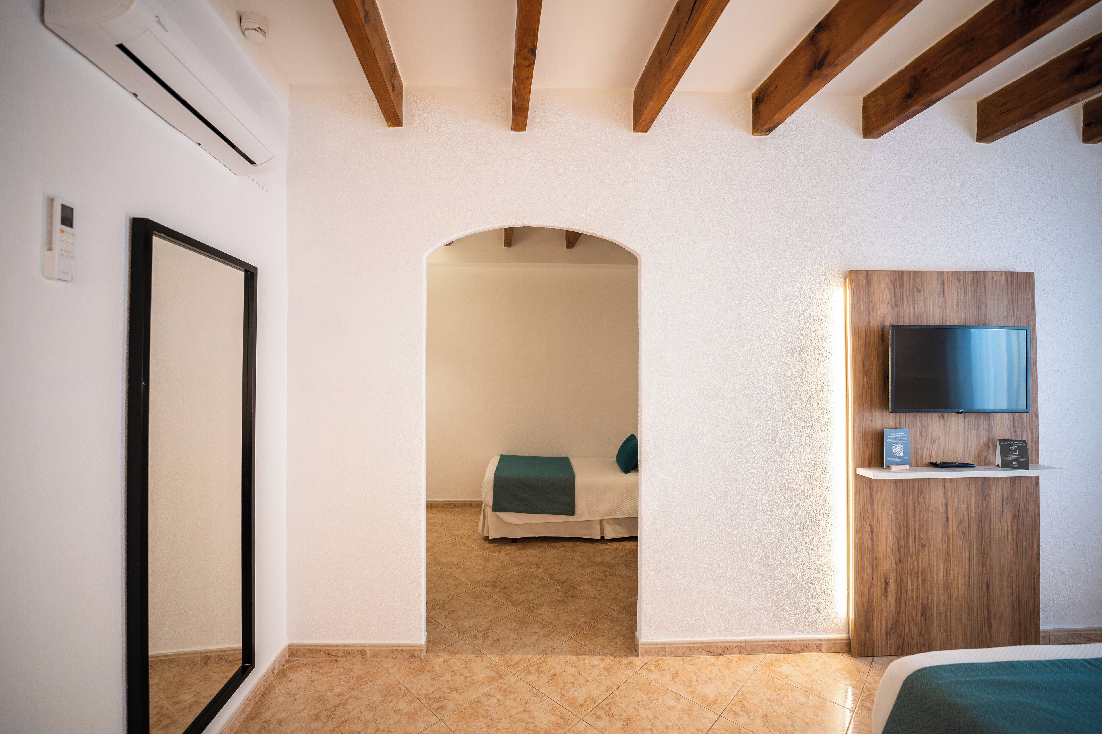 Una habitación de hotel con una cama, un televisor montado en un panel de madera y una puerta que da a otra habitación.