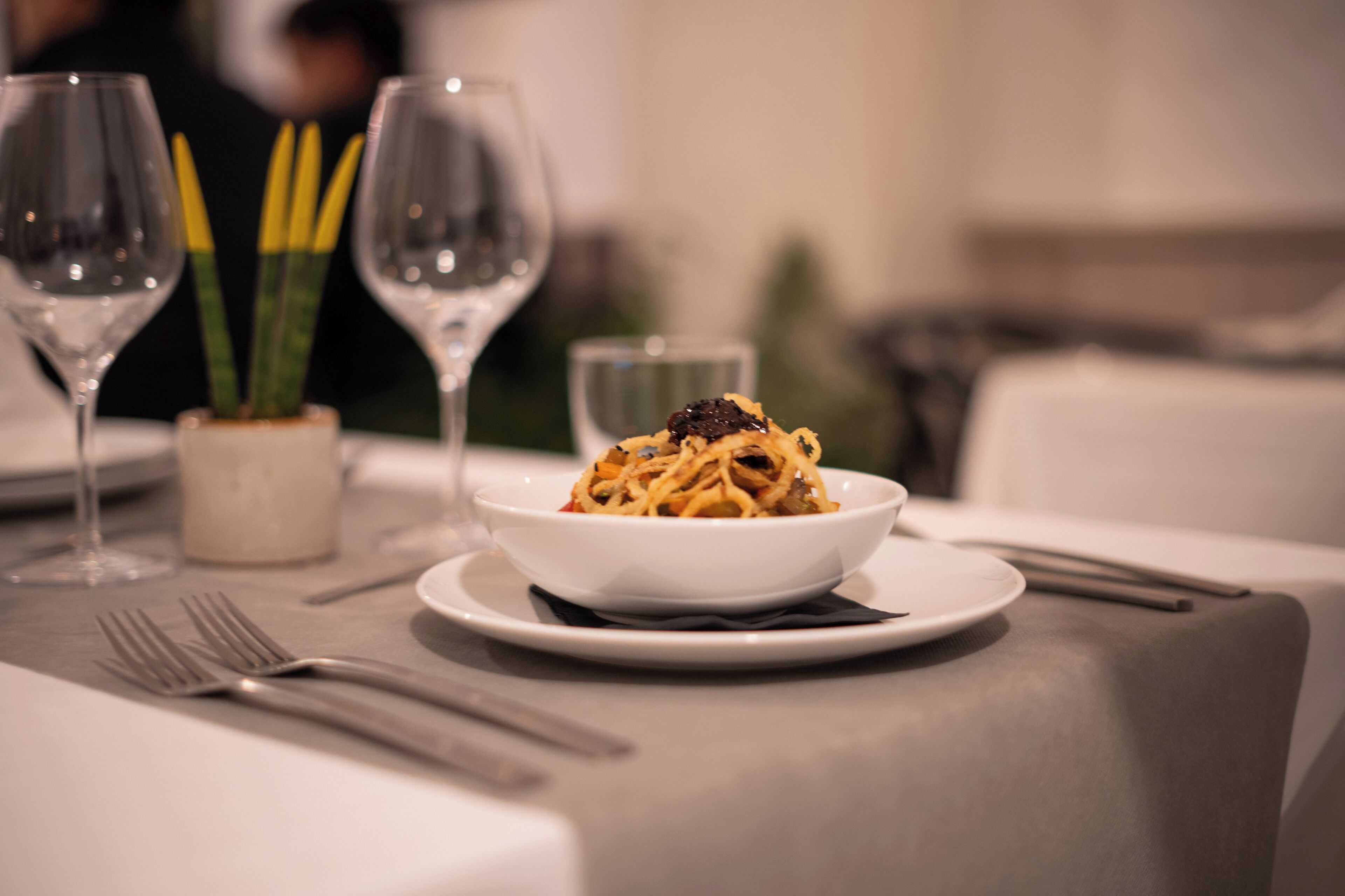 A dining table with a bowl of pasta, a glass of water, and a small potted plant.