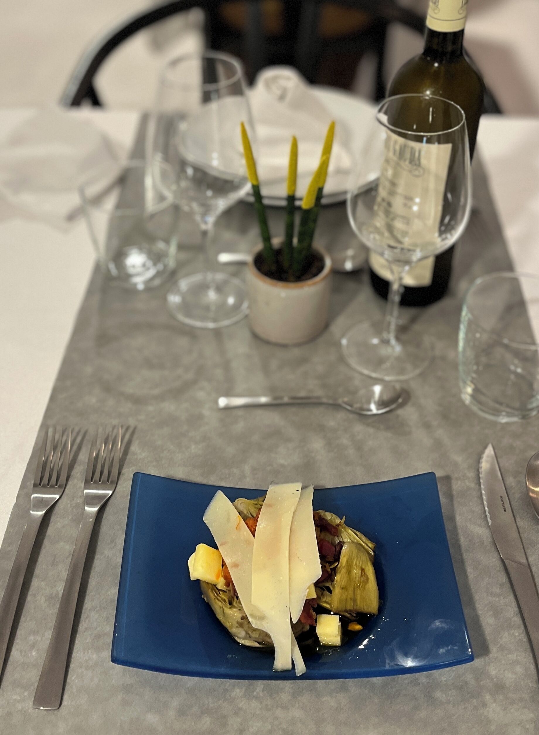 A dining table with a blue plate of food, wine glasses, and cutlery.