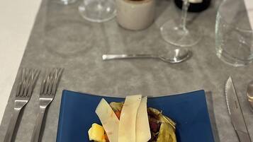 A dining table with a blue plate of food, wine glasses, and cutlery.