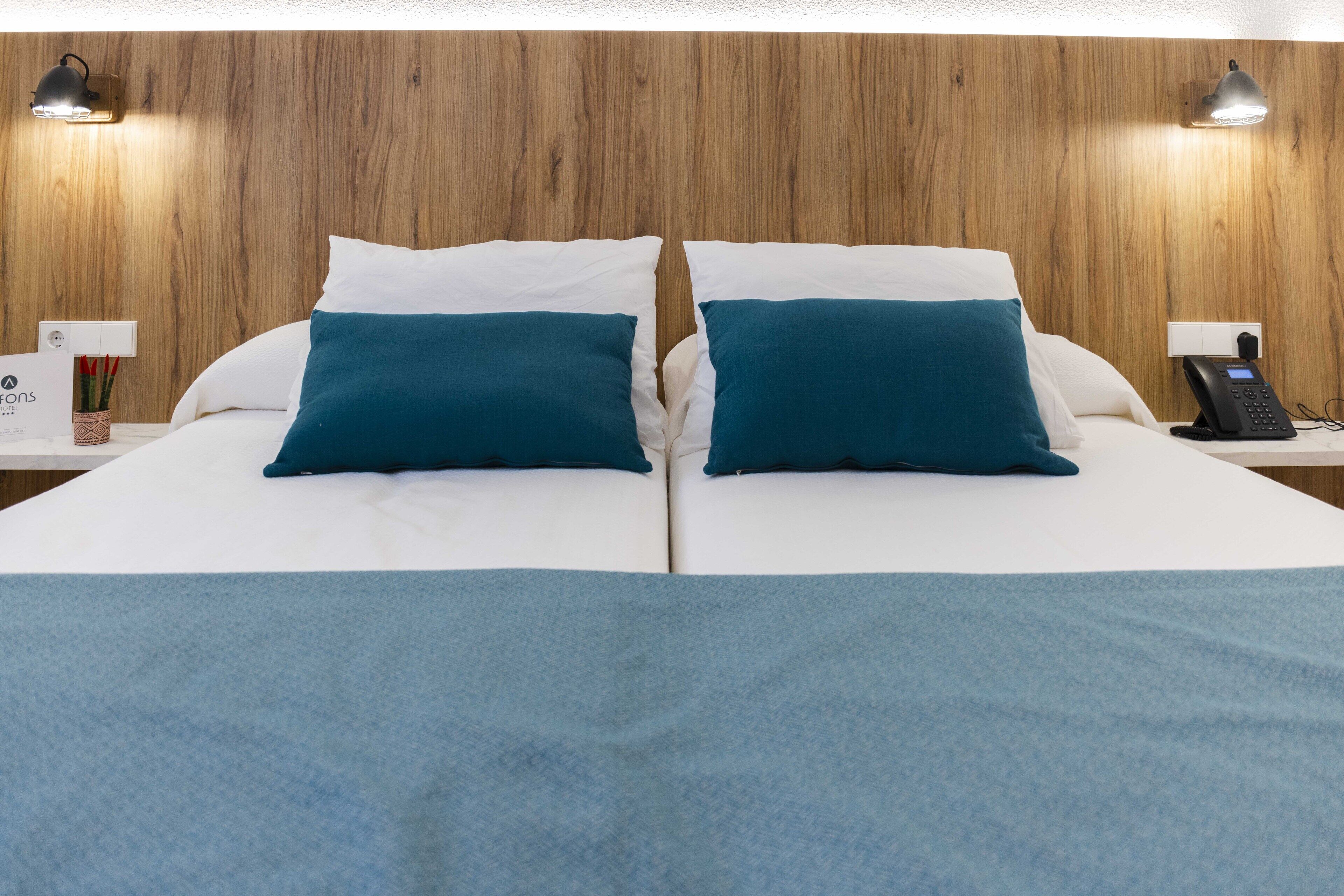 Un lit double avec des coussins de couleur turquoise, une tête de lit en bois, des tables de chevet avec des lampes et un téléphone.