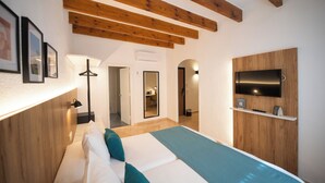 A modern hotel room with a wooden ceiling, a bed with white and teal bedding, a mounted TV, and a small shelf with a remote control. - Hotel Alfons (Ciutadella de Menorca)