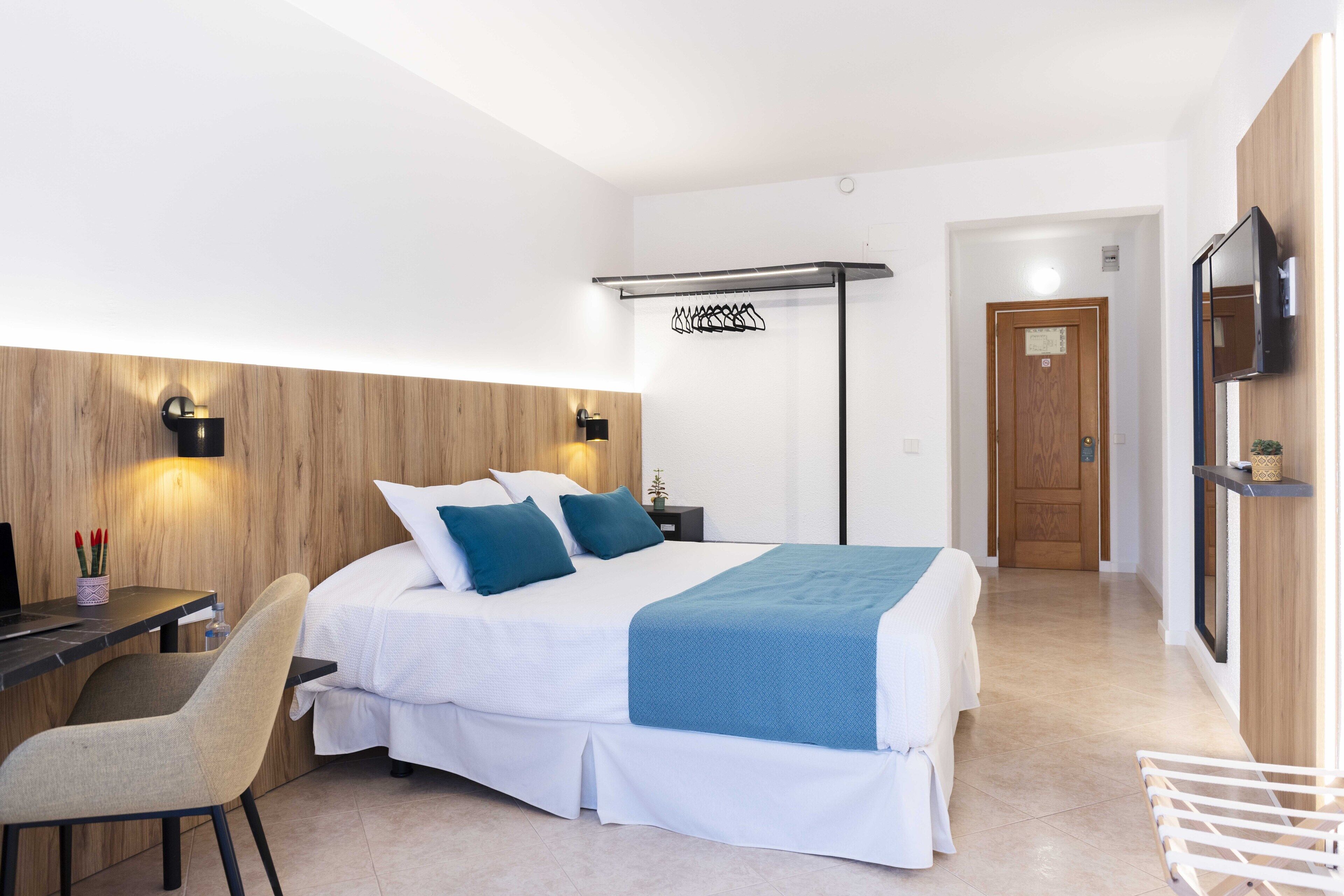 A modern hotel room with a bed, a desk, a chair, a TV, and a wooden accent wall.