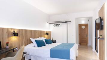 A modern hotel room with a bed, a desk, a chair, a TV, and a wooden accent wall.
