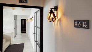 A hallway with a spa sign, a geometric wall light, and a restroom sign. - Hotel Alfons (Ciutadella de Menorca)