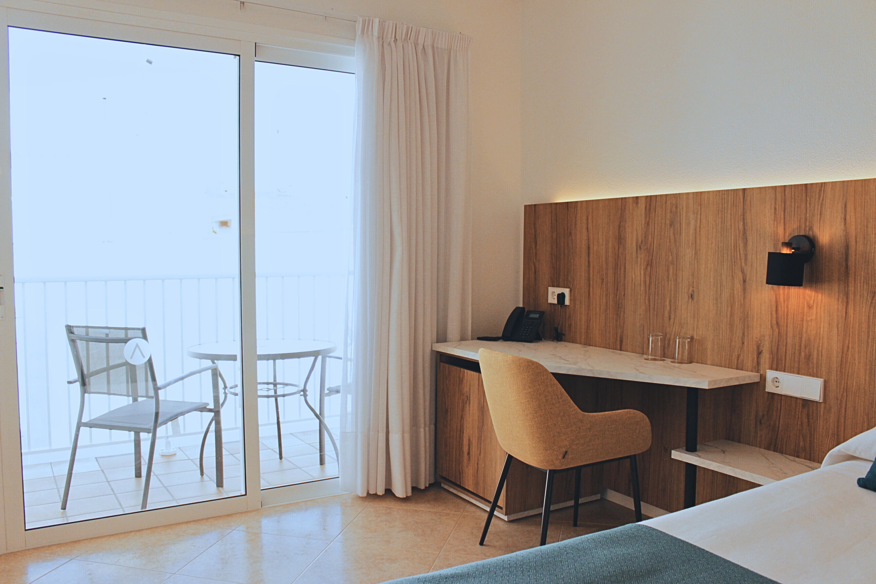 Une chambre d’hôtel comprenant un lit, un bureau, une chaise et un balcon avec une porte vitrée.