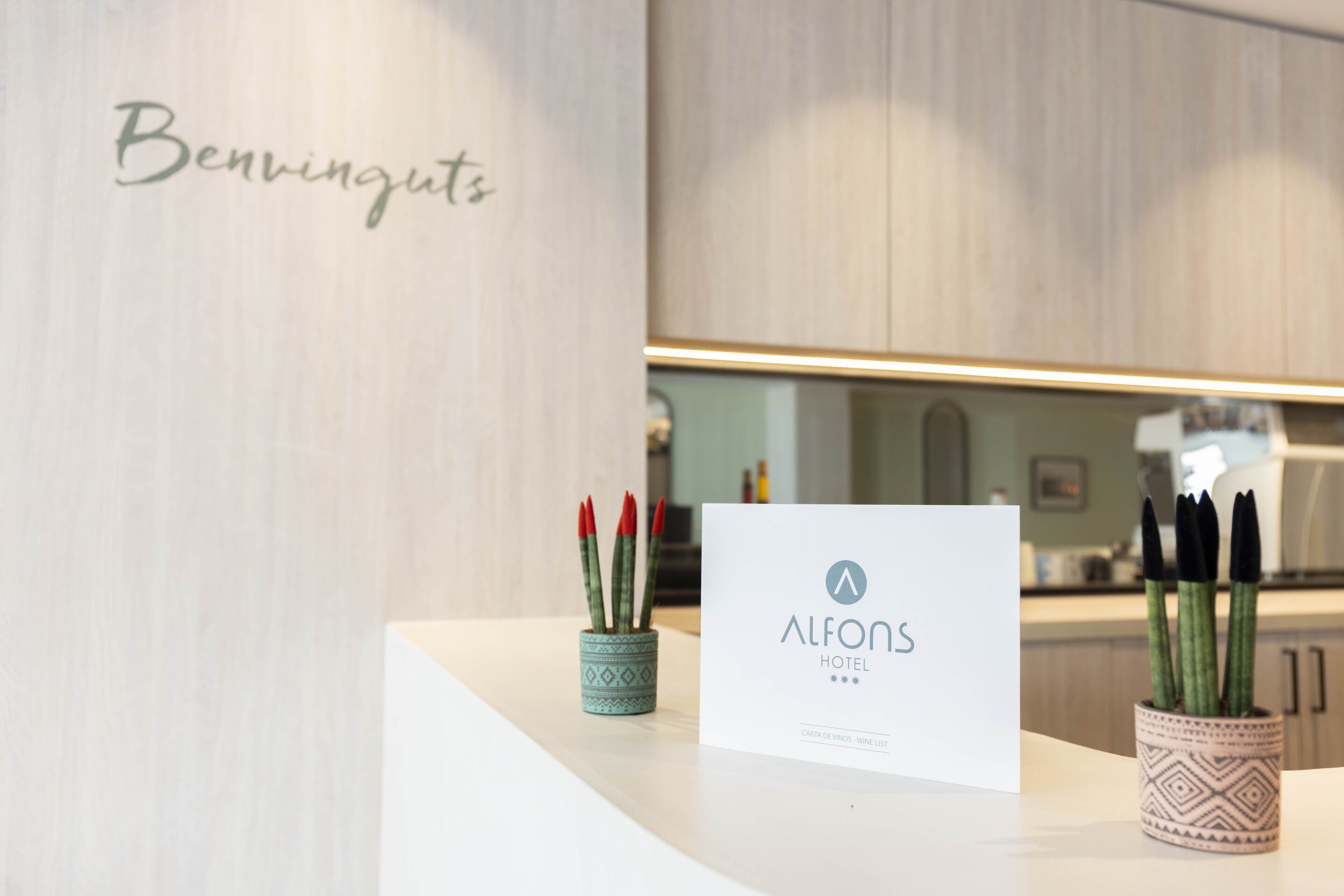 Ein Empfangstresen mit einem Schild, auf dem 'ALFONS HOTEL' steht, und einer dekorativen Vase mit Grünpflanzen.