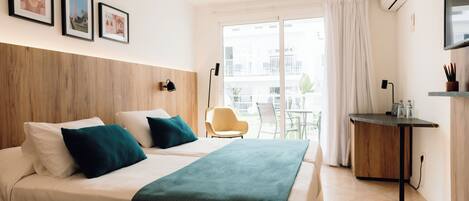Habitación de hotel con dos camas, un escritorio, una silla y un balcón con vistas a edificios.