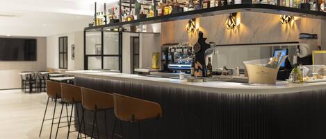 A modern bar area with a curved counter, multiple stools, and a variety of bottles and glasses.