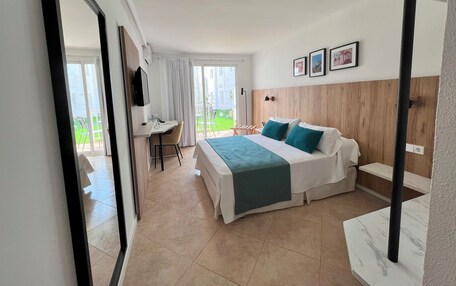 A hotel room with a bed, a desk, and a chair. There is a balcony with a view of the outside.
