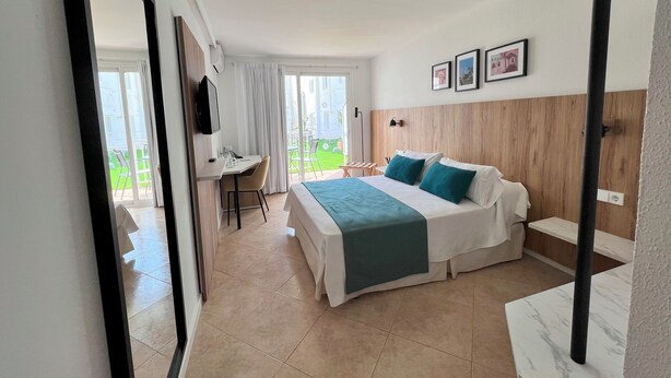 A hotel room with a bed, a desk, and a chair. There is a balcony with a view of the outside. - Hotel Alfons (Ciutadella de Menorca)
