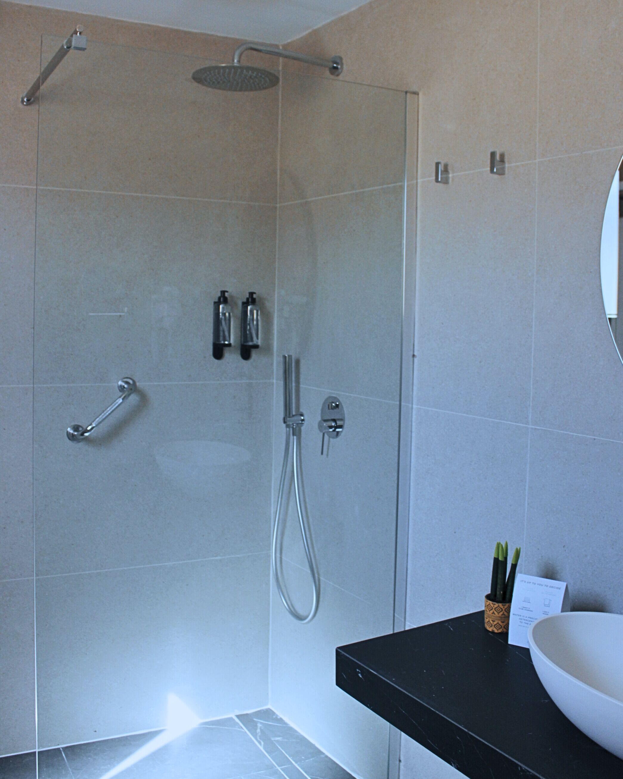 Un baño moderno con cabina de ducha de vidrio, encimera negra y lavabo blanco.