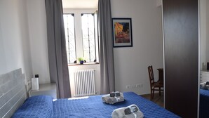 A hotel room with a large bed, a chair, a radiator, a window with curtains, and a framed picture on the wall. - Villa Campana (Torino)