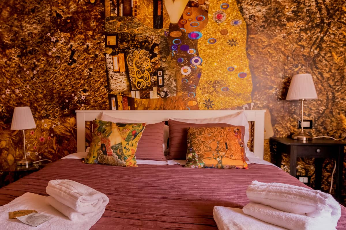 A bed with a red bedspread, multiple pillows, and two bedside lamps.