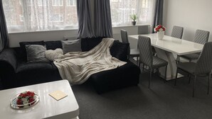 Moderni olohuone, jossa on sohva, ruokapöytä tuoleineen sekä pieni pöytä, jossa on maljakko.