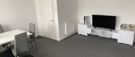 A modern living room with a white TV stand, a flat-screen TV, a white door, and a grey carpet.
