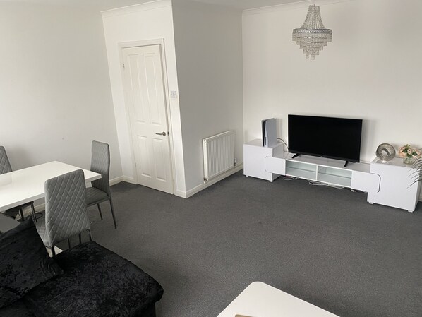 Una sala de estar moderna con un mueble blanco para el televisor, un televisor de pantalla plana, una puerta blanca y una alfombra gris.