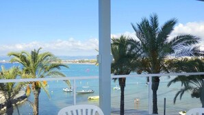 A balcony with a glass table and white chairs, overlooking a marina with boats and palm trees. - Rentalmar Acantilados Playa (Salou)