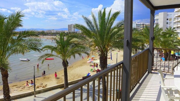 A balcony with a view of a beach, palm trees, and a clear sky. - Rentalmar Acantilados Playa (Salou)