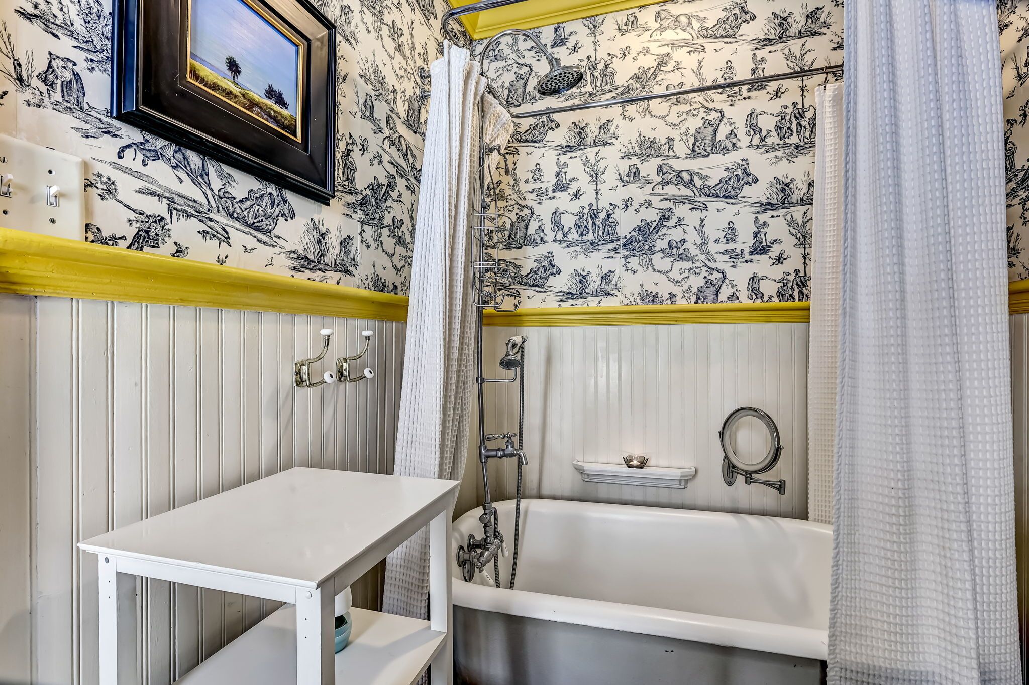 A bathroom with a bathtub, shower, and a small table.
