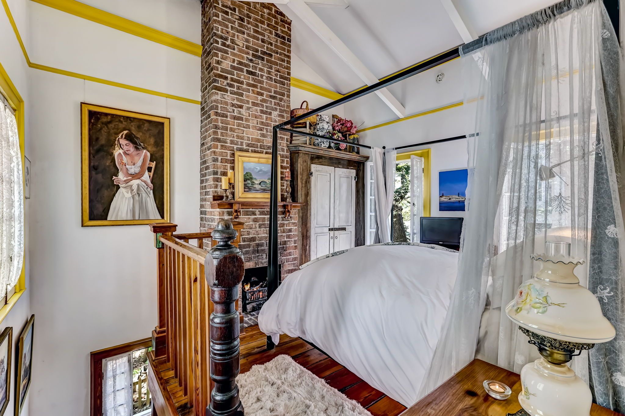 Een slaapkamer met een groot bed, een metselwerk open haard, een houten trap en uitzicht op de omgeving.