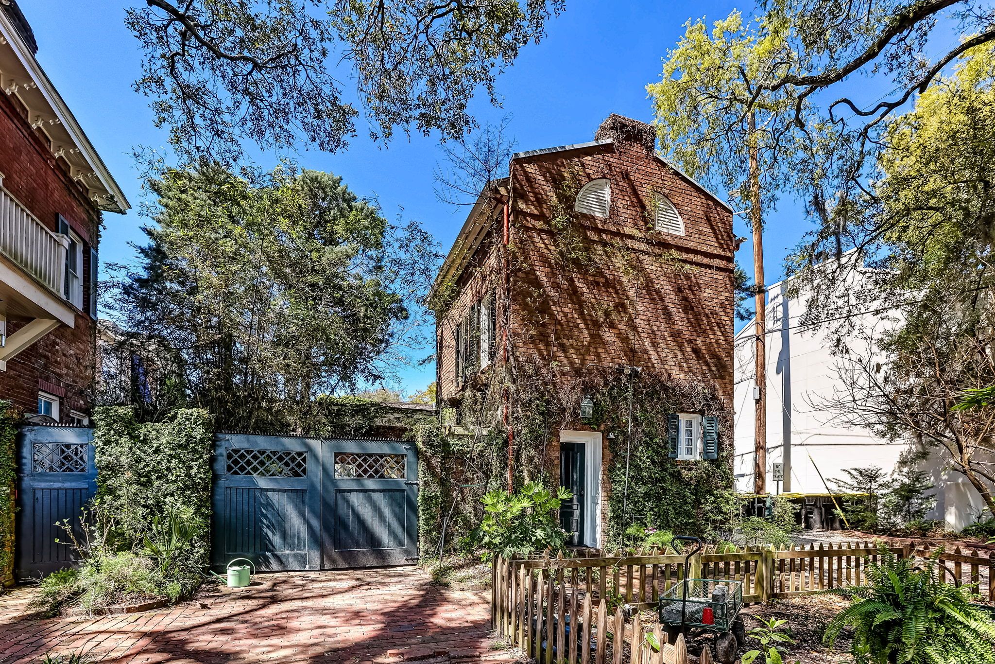 Una casa de ladrillo con cerca de madera, un jardín y cielo azul despejado.