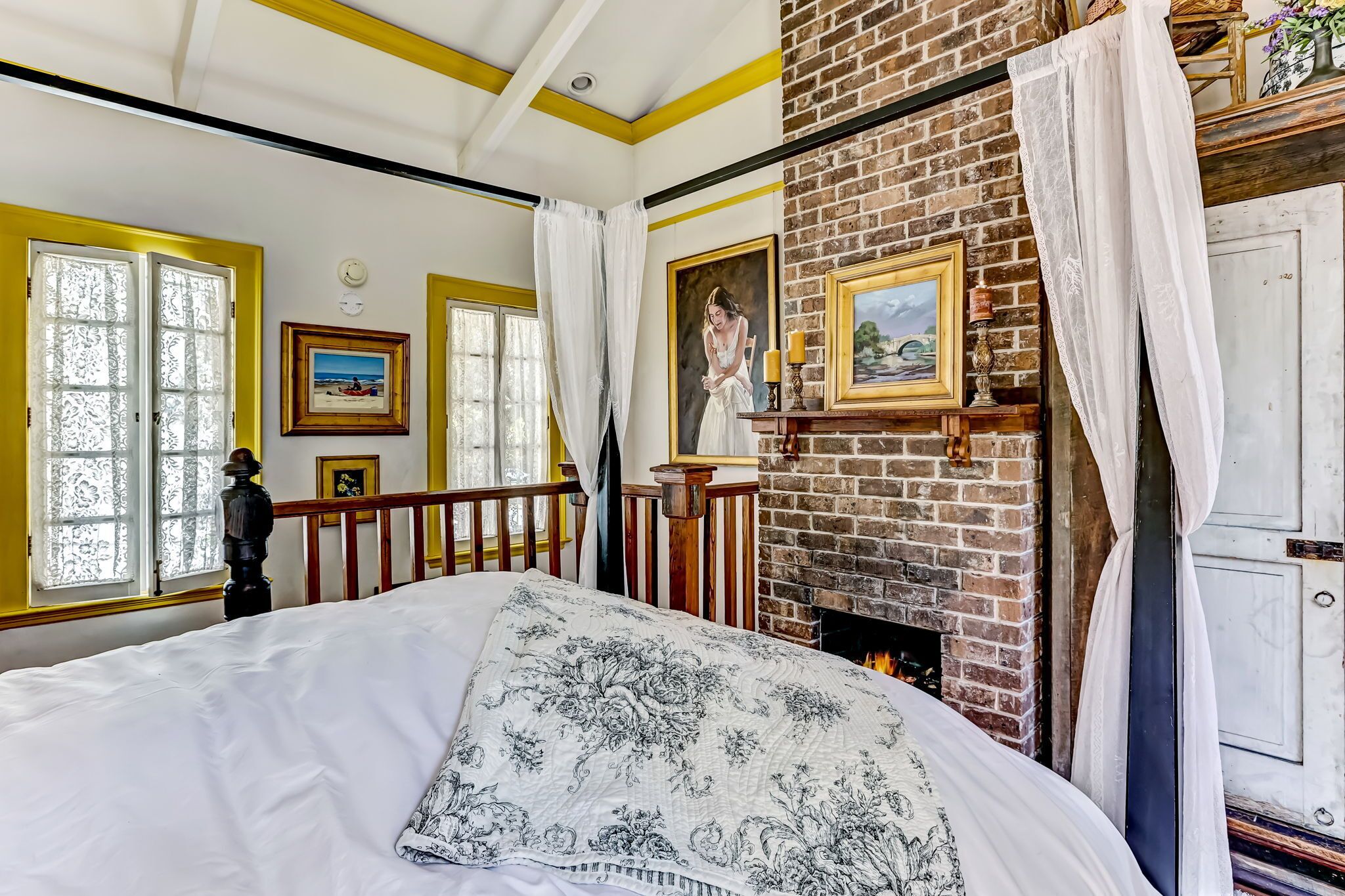 A bedroom with a large bed, a brick fireplace, and a view of the outdoors through a window.