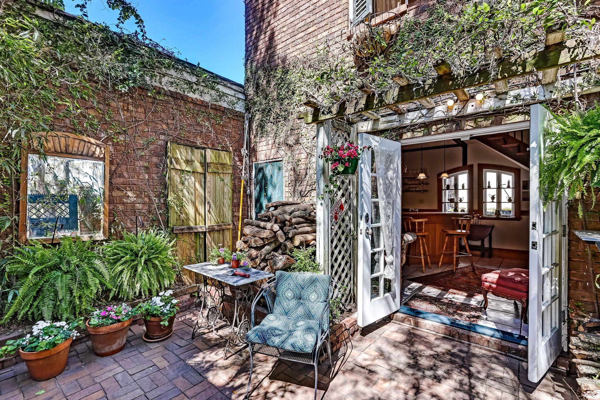 Un patio exterior acogedor con zona de comedor, plantas en macetas y una pared de ladrillo rústica.