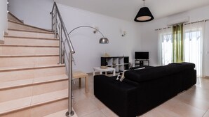 A modern living room with a staircase, a black sofa, a TV, and a lamp. - Villa with parking in the center of the village by AlgarveManta (10V3) (Manta Rota)