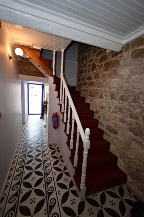 A hallway with patterned floor tiles, a wooden staircase with white balusters, and a stone wall. -  Deniz Önü Guesthouse (Ayvalik)
