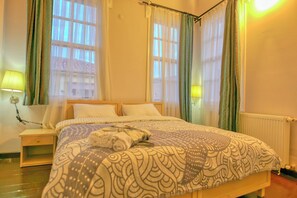 A neatly made bed with patterned bedding, a bedside table with a lamp, and a window with curtains. -  Deniz Önü Guesthouse (Ayvalik)