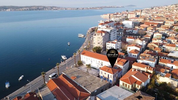 An aerial view of a coastal town with buildings along the waterfront, a clear sky, and a calm sea. -  Deniz Önü Guesthouse (Ayvalik)