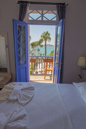 Een hotelkamer met een bed, uitzicht op zee en een balkon met een tafel en stoelen.