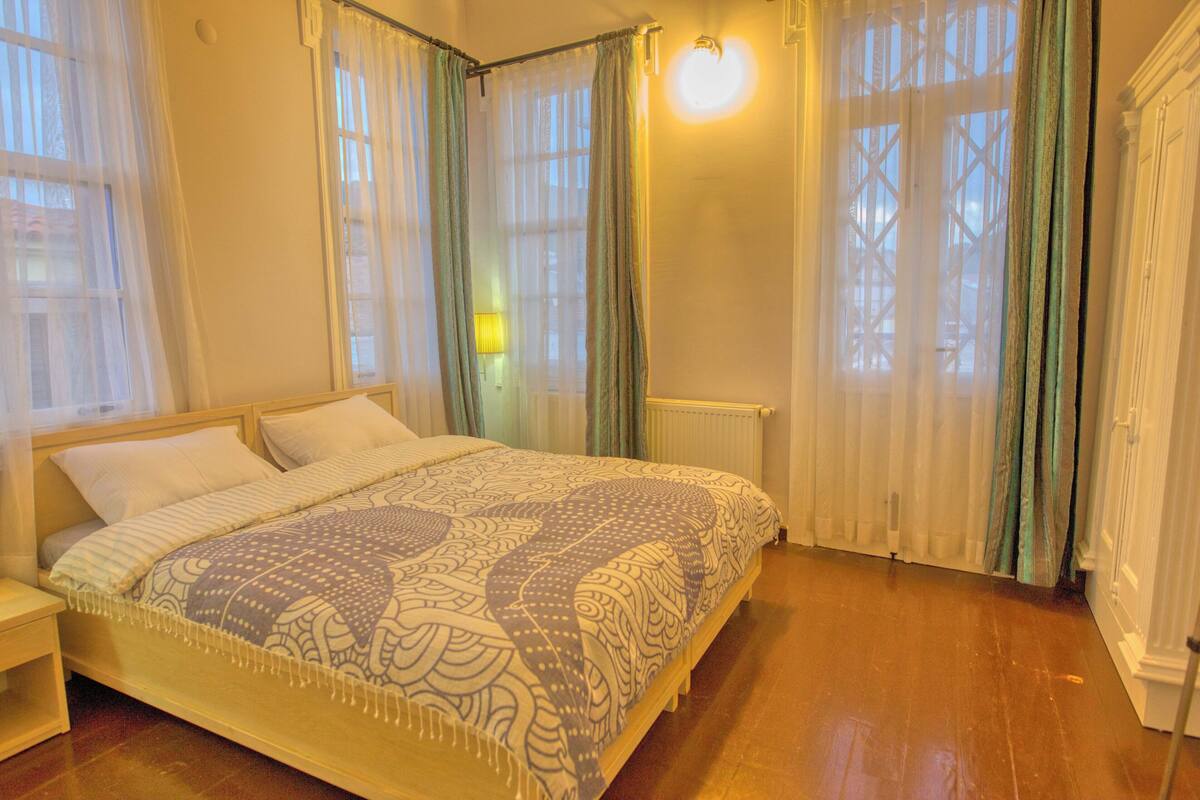 A bedroom with a wooden bed, white bedding, and a window with sheer curtains.