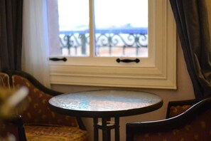 A room with a round table and a view of a balcony through a window with decorative iron railings. -  Deniz Önü Guesthouse (Ayvalik)
