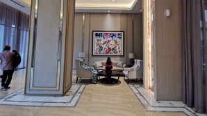 A spacious lobby with a marble floor, a large abstract painting, and a seating area with a sofa and armchairs.
