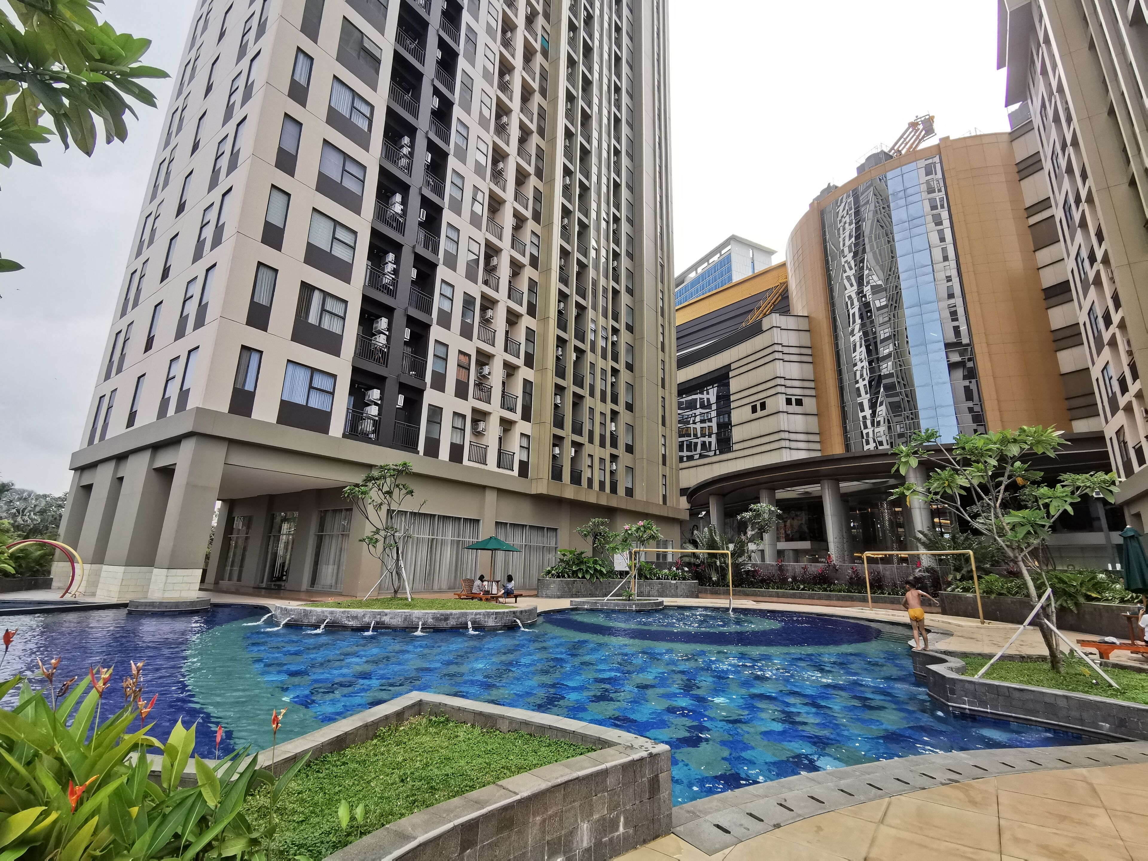 A modern high-rise building with a swimming pool surrounded by greenery.