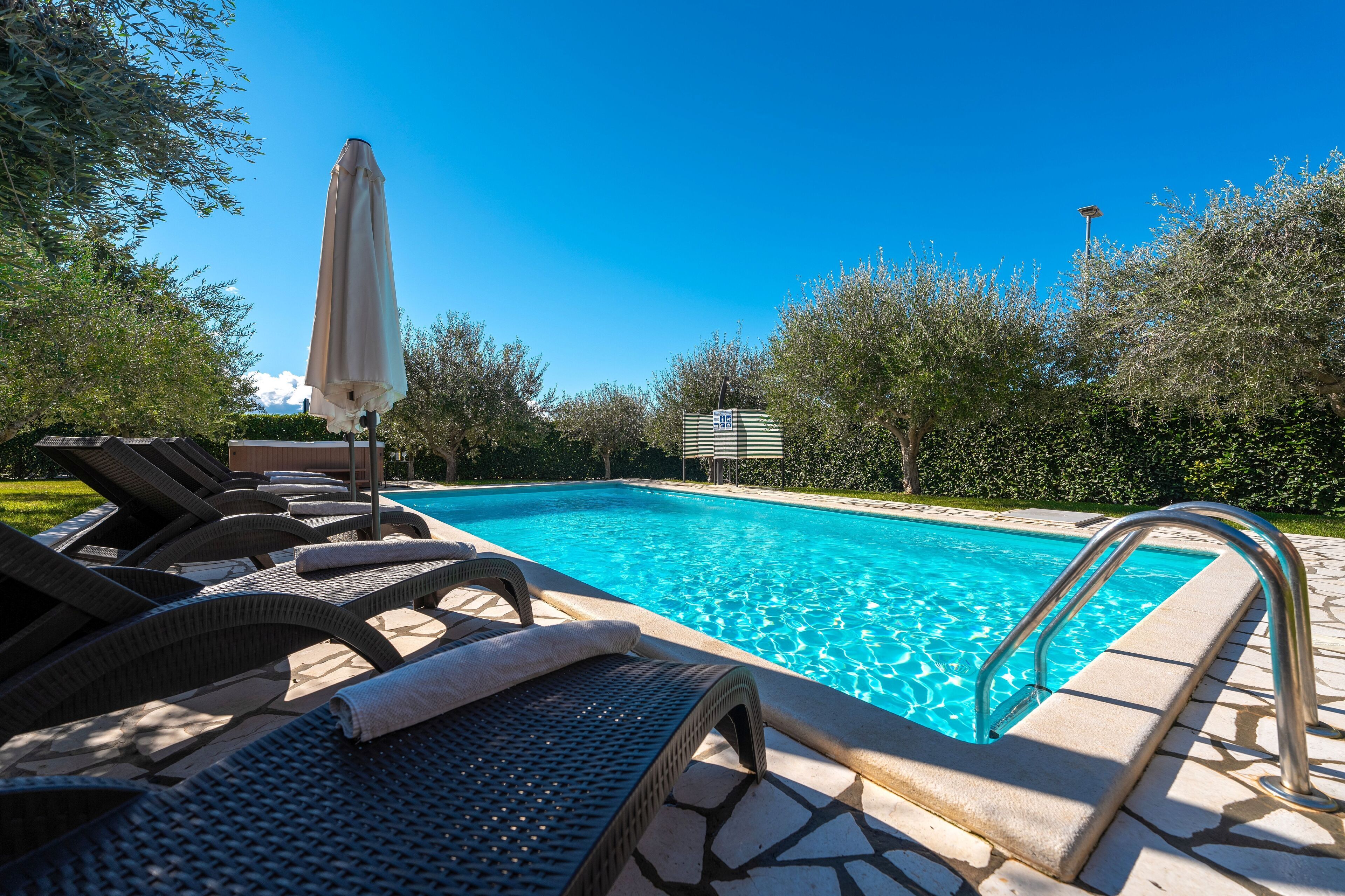 A swimming pool with lounge chairs and a sun umbrella.