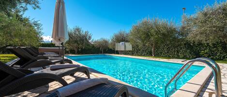 A swimming pool with lounge chairs and a sun umbrella.