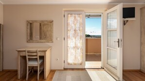 Et værelse med et træskrivebord, en stol, en dør der fører til en balkon, og et ophængt fjernsyn.
