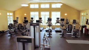 Et fitnesscenter med træningsmaskiner, styrkeområde og en stor væg med vinduer.