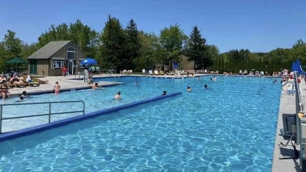 En stor udendørs swimmingpool med flere baner, omgivet af træer og en mindre bygning.