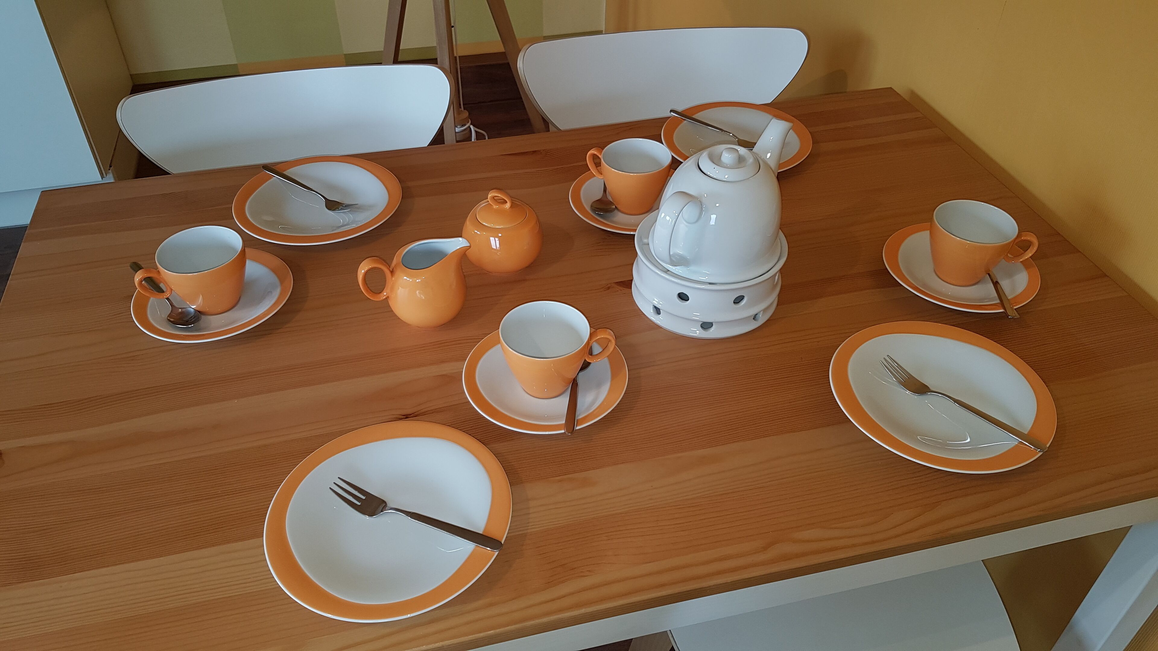 Et træspisebord dækket med orange og hvide tallerkener, kopper, en tepotte og et tesæt.