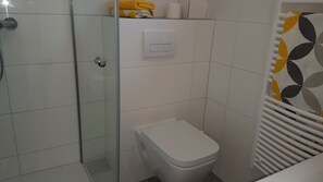 Ein Badezimmer mit Duschkabine aus Glas, Toilette und Handtuchhalter mit gefalteten Handtüchern.