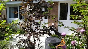 A garden area with a variety of plants and flowers, a metal chair, and a trash can.